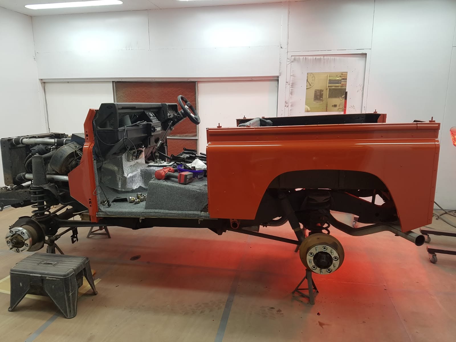 Defender tub and bulkhead resprayed in bright orange, part-way through reassembly in the booth